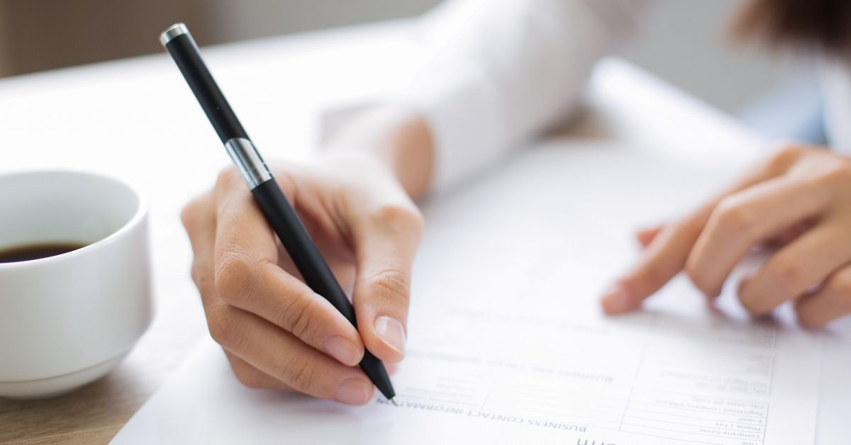 Person filling out a form with a cup of coffee.