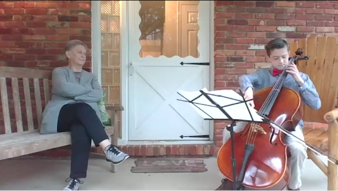 Boy playing cello on front porch next to grandmother