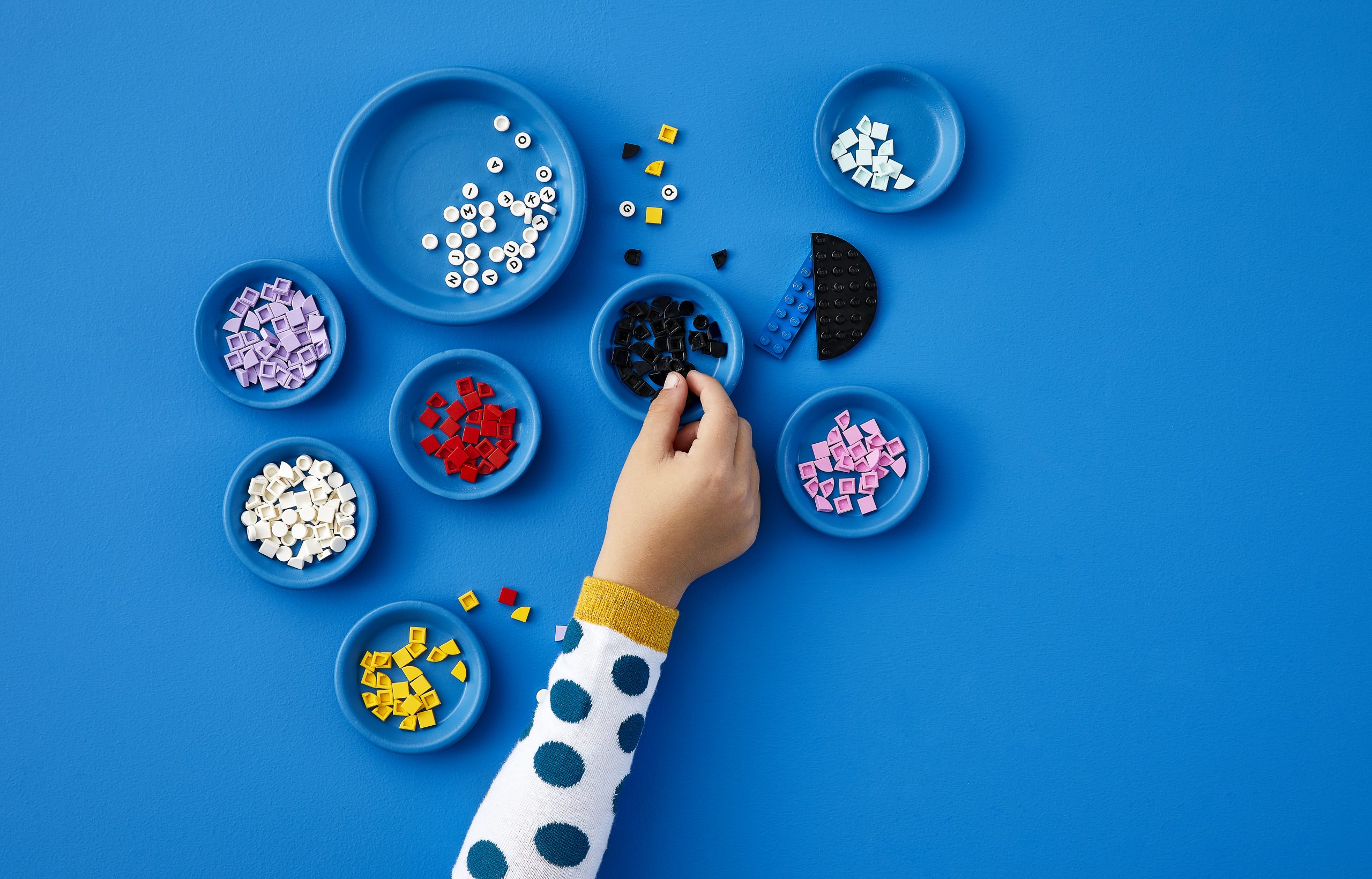 Photo of a child's hand and several piles of different colors Legos over a blue background.