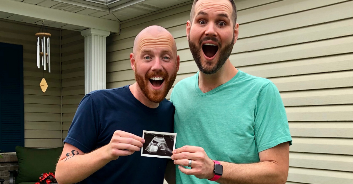 Two men in front of a house holding a photo from an ultrasound