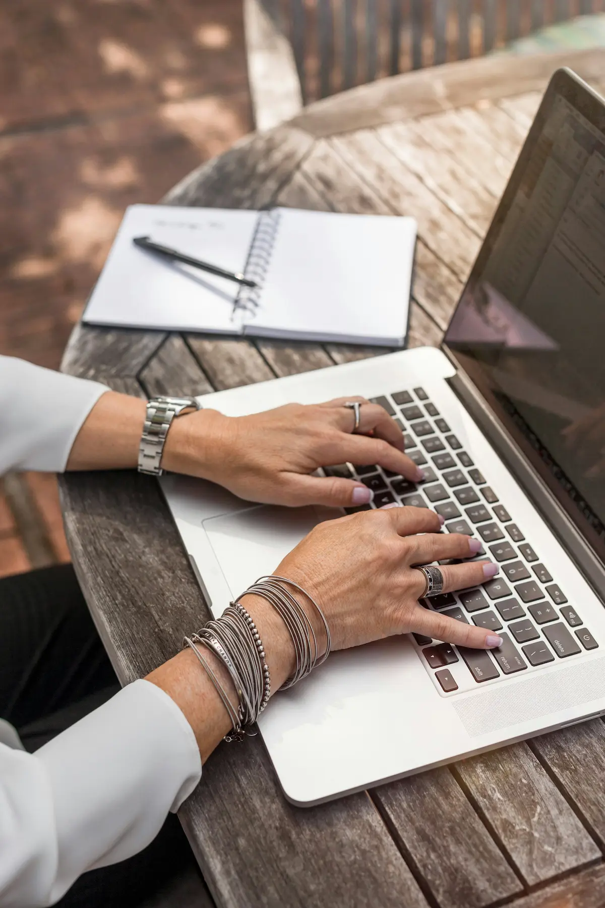 Hands typing on a laptop with a notebook in the background