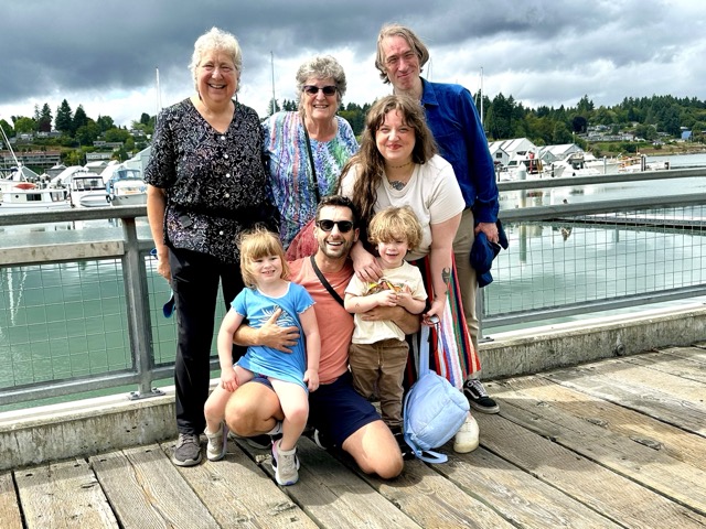 A family with two grandparents, three adults, and two children pose on a dock.